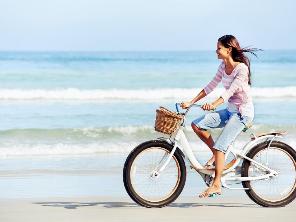 woman riding bike on beach by water