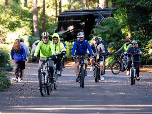 Group of cyclists in light jackets riding along a tree-lined road at Hilton Head Island Motorcoach Resort