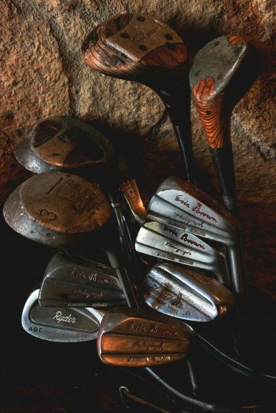 Vintage wooden golf clubs leaning against a stone wall