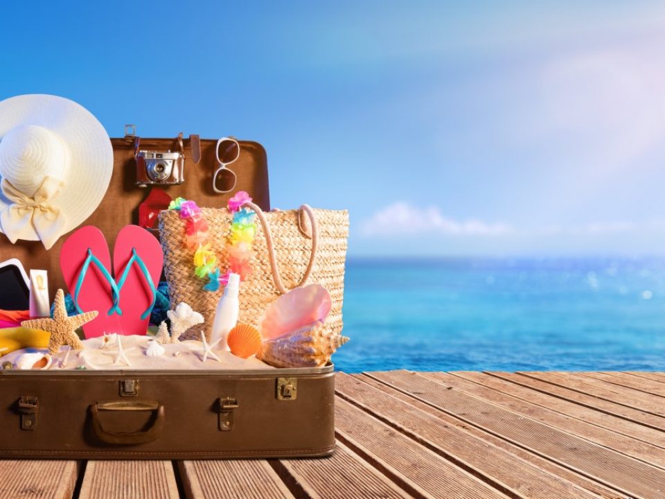 suitcase with beach items beside water